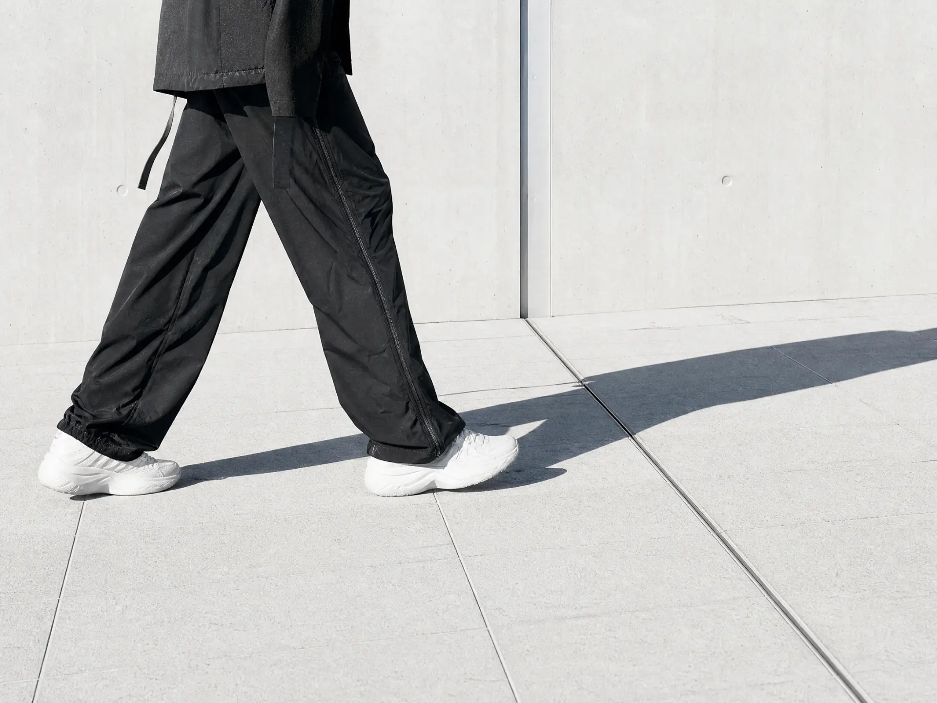 Cropped figure walking past a pale concrete wall