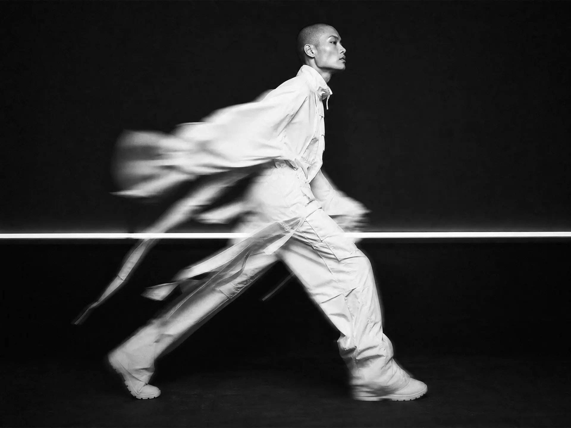 A figure in white moving through a black studio in long exposure